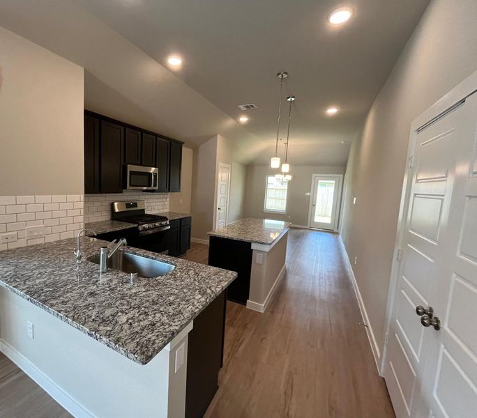 A modern kitchen with granite countertops, dark cabinets, and sleek stainless appliances.