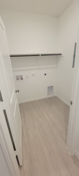A spacious laundry room with light wood flooring and sleek wall shelving, designed for modern convenience.