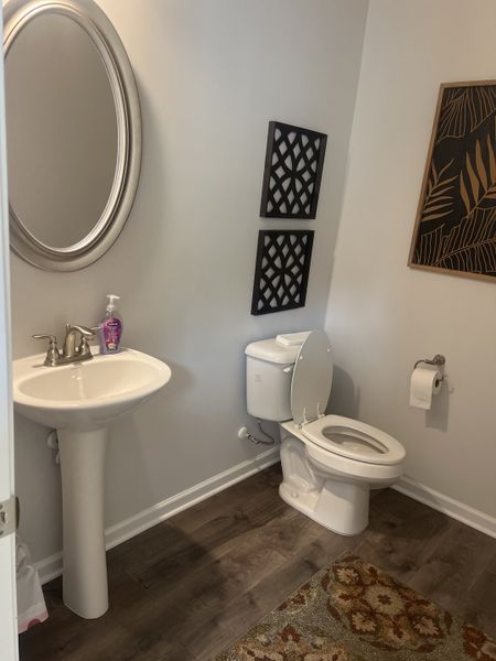 A cozy bathroom featuring a pedestal sink, elegant mirror, and dark wood flooring with decorative wall accents. A cozy bathroom featuring a pedestal sink, elegant mirror, and dark wood flooring with decorative wall accents.