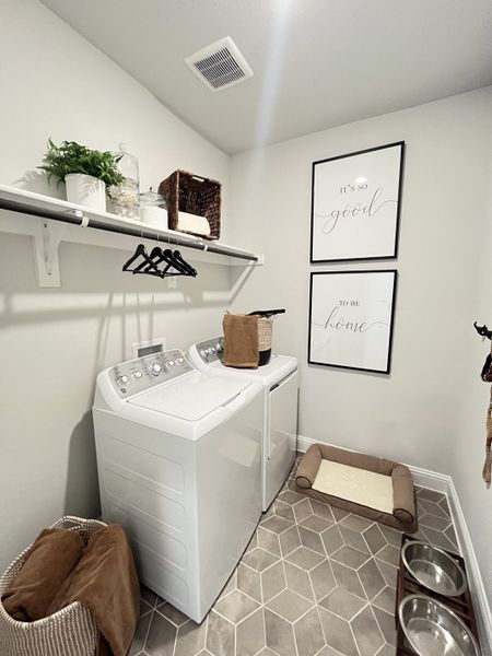 A chic laundry room with modern appliances, geometric tile, wall decor, and pet amenities for stylish functionality.