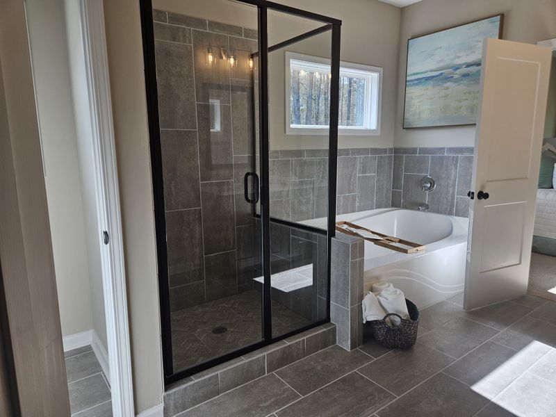  A spacious bathroom featuring a glass-enclosed shower, bathtub, and a large window for natural light.