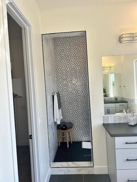 A modern bathroom featuring geometric tile shower, sleek vanity, and elegant lighting.