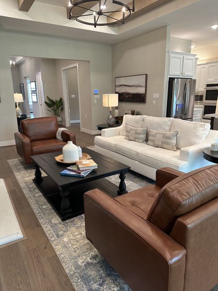 A cozy living room featuring leather chairs, a white sofa, and a dark coffee table under a stylish chandelier.