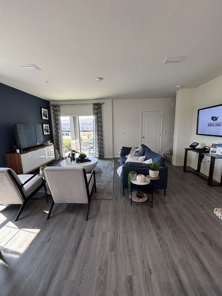 A spacious living room with navy accent walls, sleek flooring, and abundant natural light in Avian Pointe Townhomes by D.R. Horton (Apopka, FL).