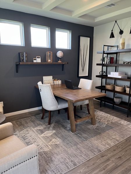 A modern office with a wooden desk, cozy chairs, dark accent wall, and elegant shelving creates a stylish, productive space.