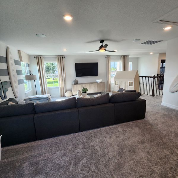 A cozy living room with a plush gray sofa, wall-mounted TV, and large windows providing ample natural light.