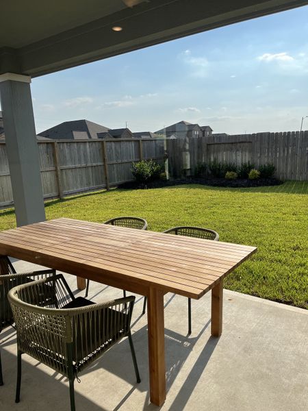A cozy outdoor patio with a wooden table and chairs, overlooking a well-maintained grassy backyard.