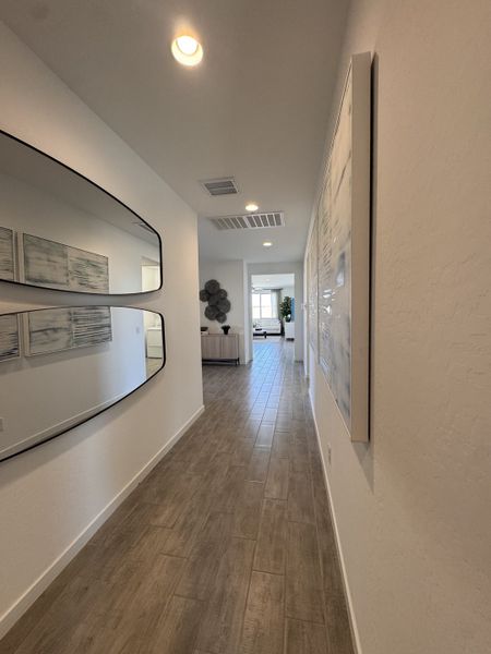 A modern hallway with wood-style flooring, sleek mirrors, and elegant artwork, leading to a bright living space.