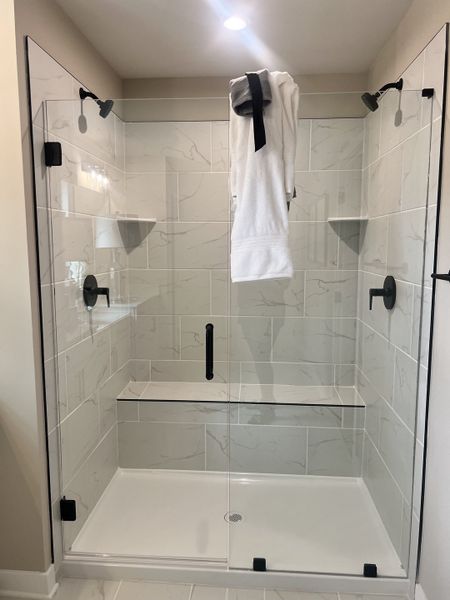 A sleek glass shower with marble tiles, dual showerheads, and a built-in bench for ultimate relaxation.