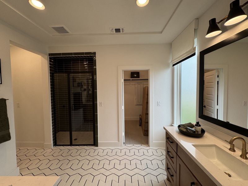 A modern bathroom featuring herringbone tile flooring, dual sinks, a sleek black-tiled shower, and elegant lighting. A modern bathroom featuring herringbone tile flooring, dual sinks, a sleek black-tiled shower, and elegant lighting.