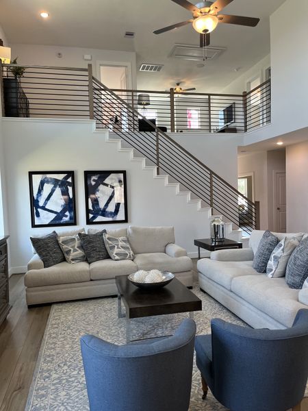 A modern living room with plush sofas, abstract art, and a sleek open staircase leading to an airy loft space.