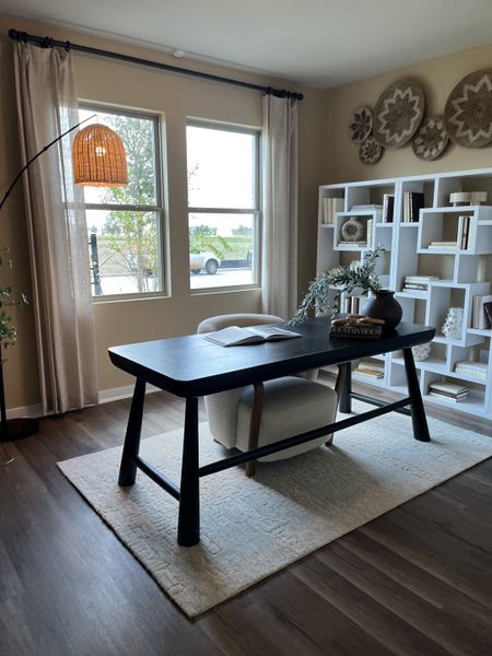 A cozy home office with a sleek black desk, woven decor, and ample natural light, complemented by a stylish bookshelf.