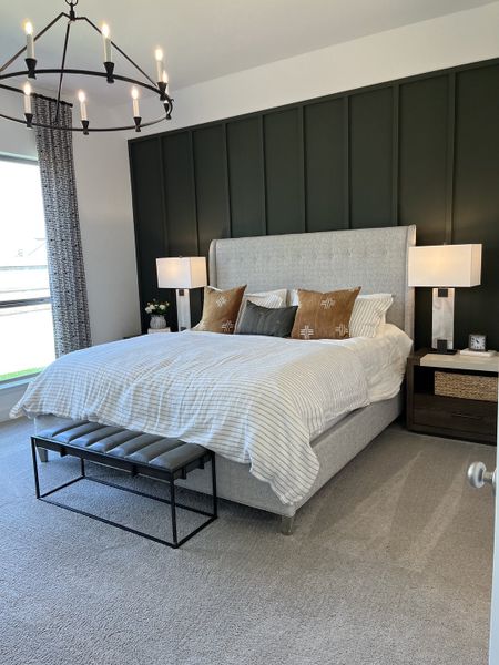 A modern bedroom featuring a tufted headboard, dark accent wall, elegant chandelier, and cozy decor.