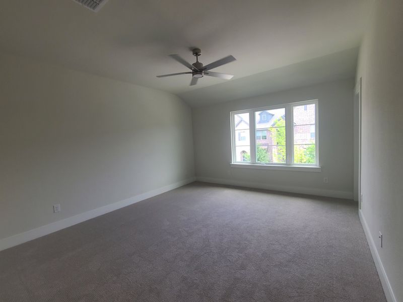 A spacious bedroom with neutral carpet, large window, and ceiling fan, offering a bright, airy atmosphere.