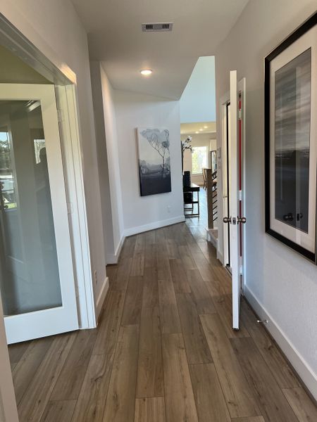A sleek hallway with wood flooring, modern art, and recessed lighting leads to an airy living space.