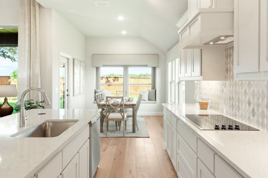 White kitchen with quartz countertops and cooktop opening to a breakfast nook with dining table and large windows White kitchen with quartz countertops and cooktop opening to a breakfast nook with dining table and large windows