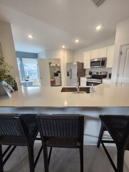 A sleek kitchen featuring stainless steel appliances, white cabinetry, and a spacious island with woven barstools.