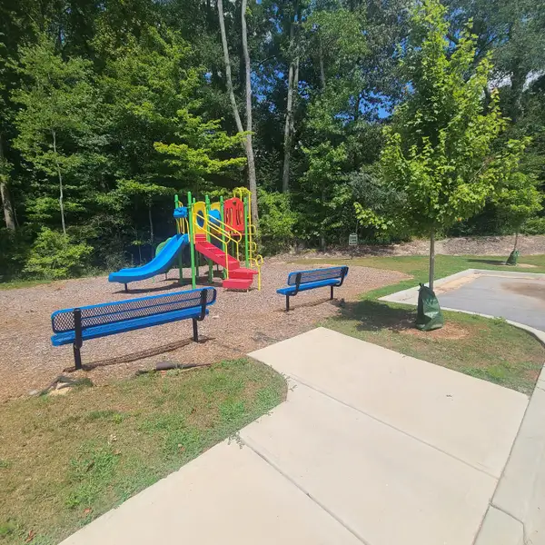 Colorful playground with blue benches and lush trees in Paces Estates by McKinley Homes (Lithia Springs, GA).