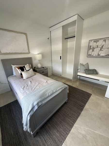 A cozy bedroom featuring a sleek gray bed, minimalist decor, and ample natural light, creating a serene atmosphere.