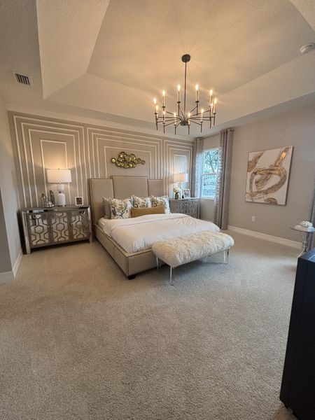 Stylish bedroom with tray ceiling, chandelier, plush bedding, and contemporary decor.