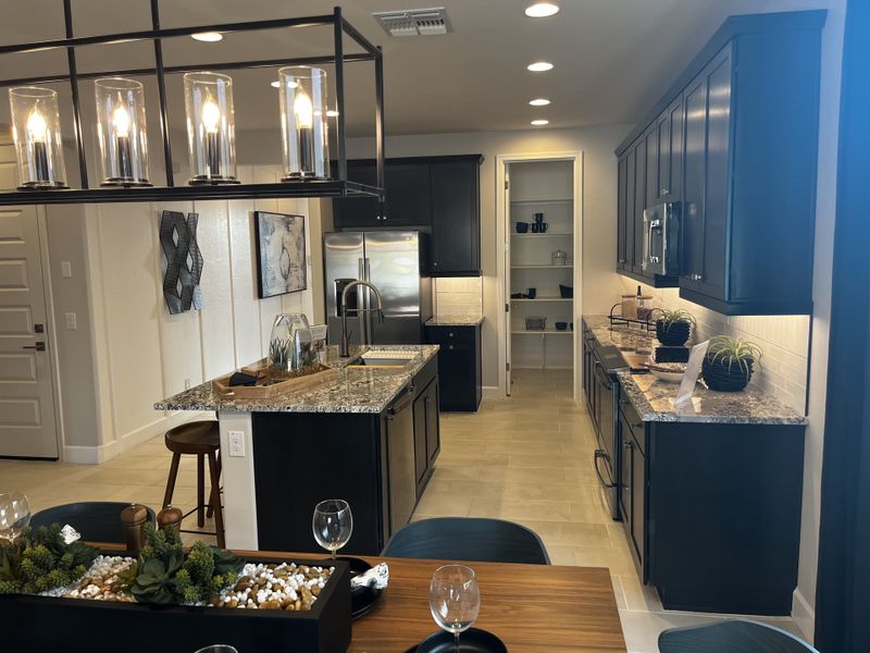 A modern kitchen with dark cabinetry, pendant lighting, and a central island with seating.