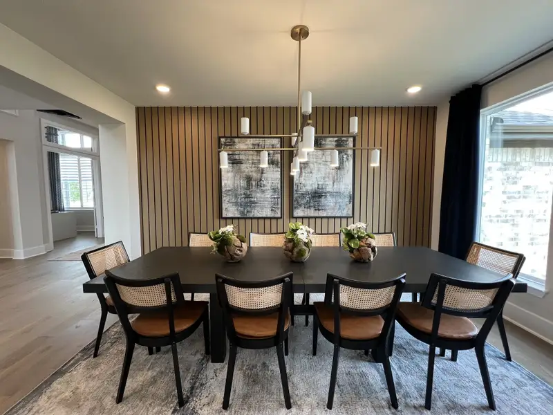 A modern dining room featuring a sleek black table, stylish chairs, and contemporary lighting with an accent wall.