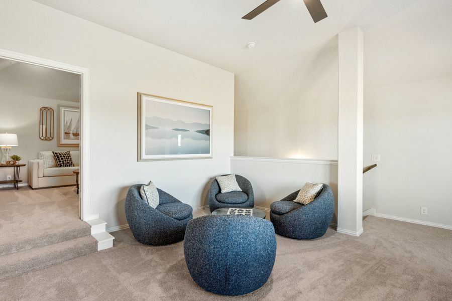 Upstairs loft sitting area with three blue round chairs, ottoman, ceiling fan, and carpet flooring