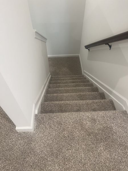 A carpeted stairway with sleek white walls and a dark wooden handrail for a modern touch. A carpeted stairway with sleek white walls and a dark wooden handrail for a modern touch.