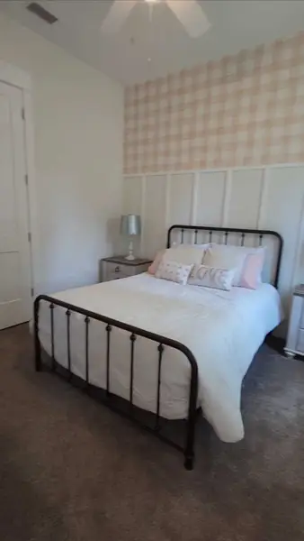 A cozy bedroom featuring a black metal bed, soft bedding, and accent pillows against a checkered feature wall.