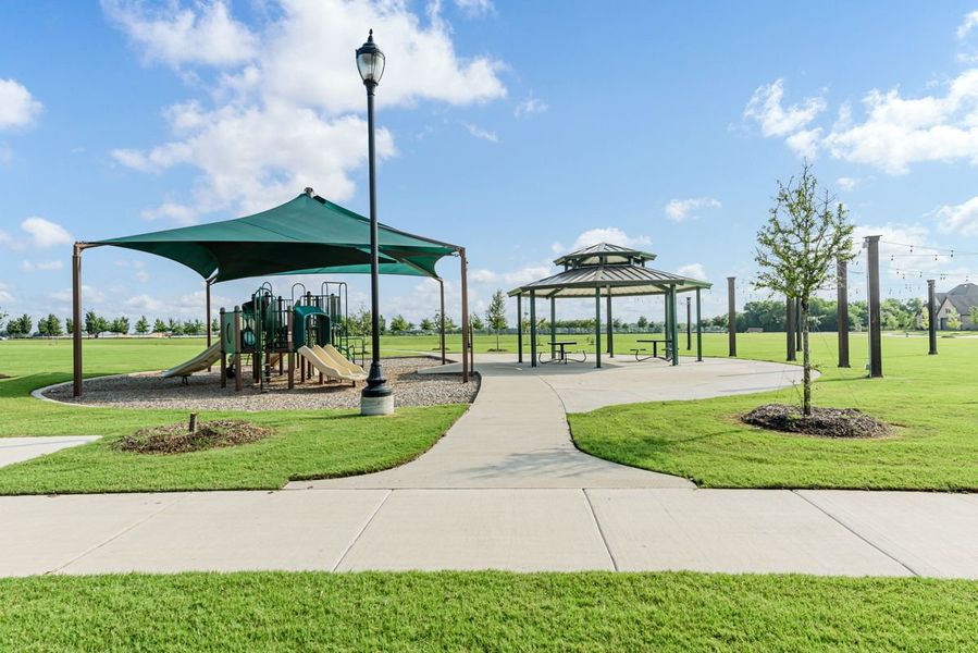 Community park with shaded playground, gazebo with picnic tables, and concrete walking path on green lawn Community park with shaded playground, gazebo with picnic tables, and concrete walking path on green lawn