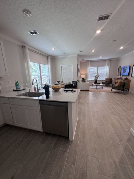 An open-concept living area with wood-like floor tiles, a modern kitchen island, and ample natural light.