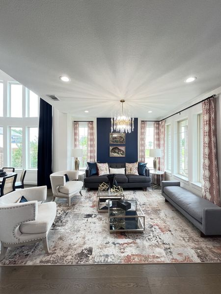 A luxurious living room with elegant seating, a chic chandelier, and large windows, featuring a modern navy accent wall.