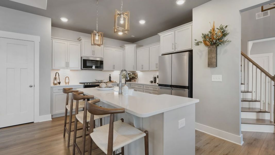 Kitchen featuring white quartz countertops, crown molding, modern furniture, and LVP at Village at Midway by DRB Homes Kitchen featuring white quartz countertops, crown molding, modern furniture, and LVP at Village at Midway by DRB Homes