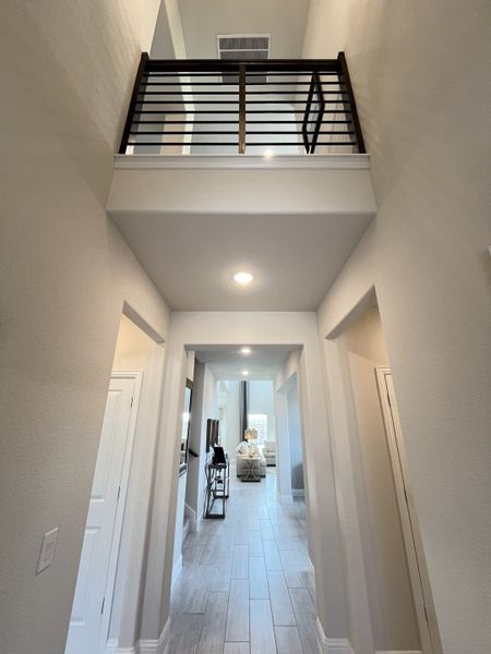 A bright hallway with sleek flooring, recessed lighting, and a modern railing leads to a cozy living area.