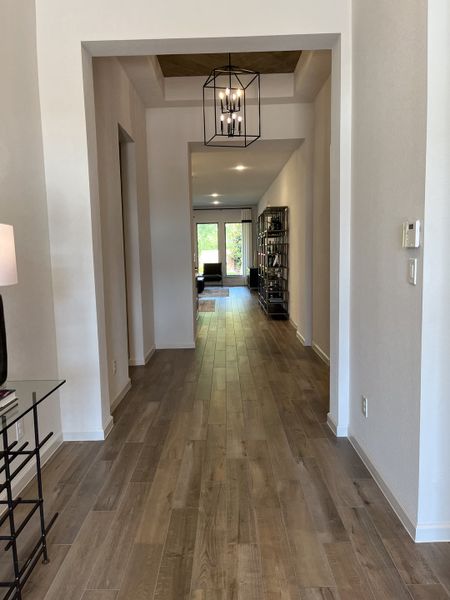 A modern hallway with elegant wood flooring, statement lighting, and a view to a bright living area. A modern hallway with elegant wood flooring, statement lighting, and a view to a bright living area.