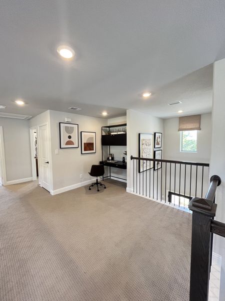 A cozy loft area with a built-in desk, art decor, and carpeted flooring, perfect for a small office or reading nook.