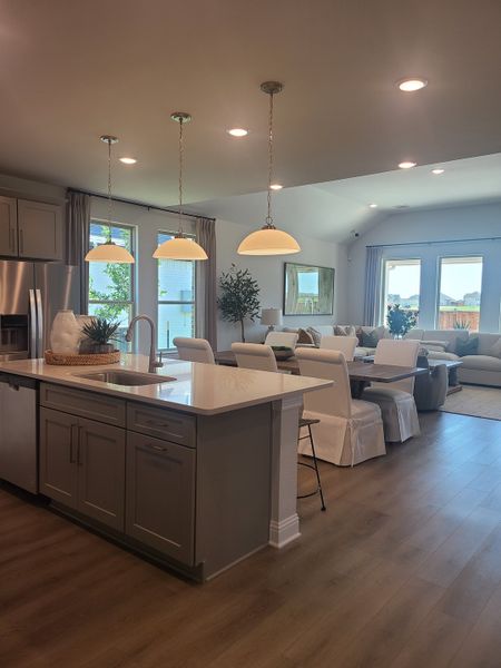A modern open-concept kitchen and living area with pendant lighting, sleek cabinetry, and elegant flooring.