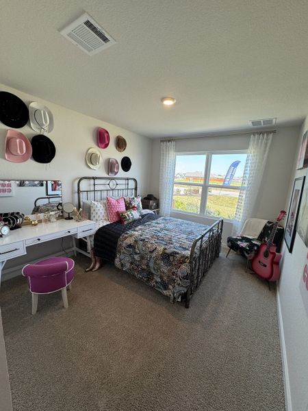 A cozy bedroom with a decorative hat display, comfy bed, vibrant decor, and bright window views.