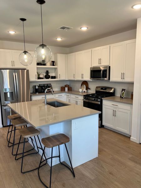 A modern kitchen with sleek white cabinets, stainless steel appliances, and a large island with pendant lighting.