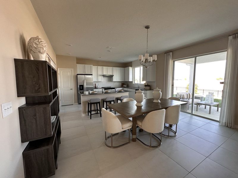 A spacious open-concept kitchen and living area featuring wood cabinetry, granite countertops, and warm-toned flooring in Landings at Lake Mabel Loop by KB Home (Dundee, FL).