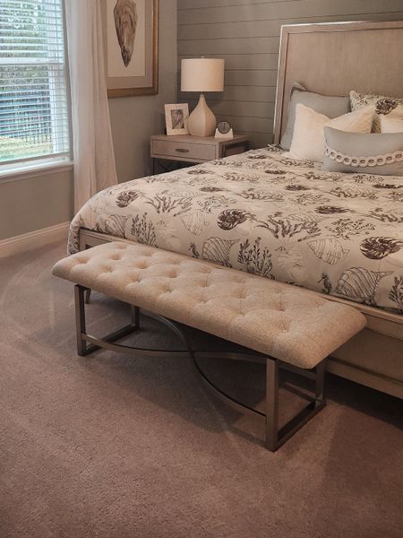 A cozy bedroom with coastal-themed bedding, tufted bench, and elegant side table with soft lighting. A cozy bedroom with coastal-themed bedding, tufted bench, and elegant side table with soft lighting.
