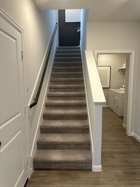 A modern staircase with carpeted steps, sleek railings, and adjacent laundry room, set in a crisp, neutral-toned hallway. A modern staircase with carpeted steps, sleek railings, and adjacent laundry room, set in a crisp, neutral-toned hallway.