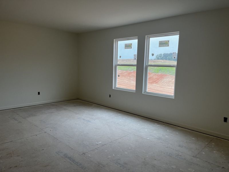 A sunlit, unfinished room featuring two large windows and neutral walls, ready for personal touches and flooring.