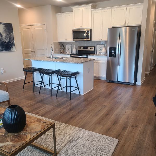 A modern kitchen with white cabinetry, granite island, and stainless appliances, featuring elegant wood flooring. A modern kitchen with white cabinetry, granite island, and stainless appliances, featuring elegant wood flooring.