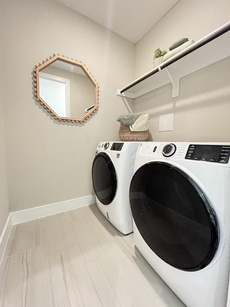 A chic laundry room with modern washer and dryer, neutral tile, and geometric mirror.