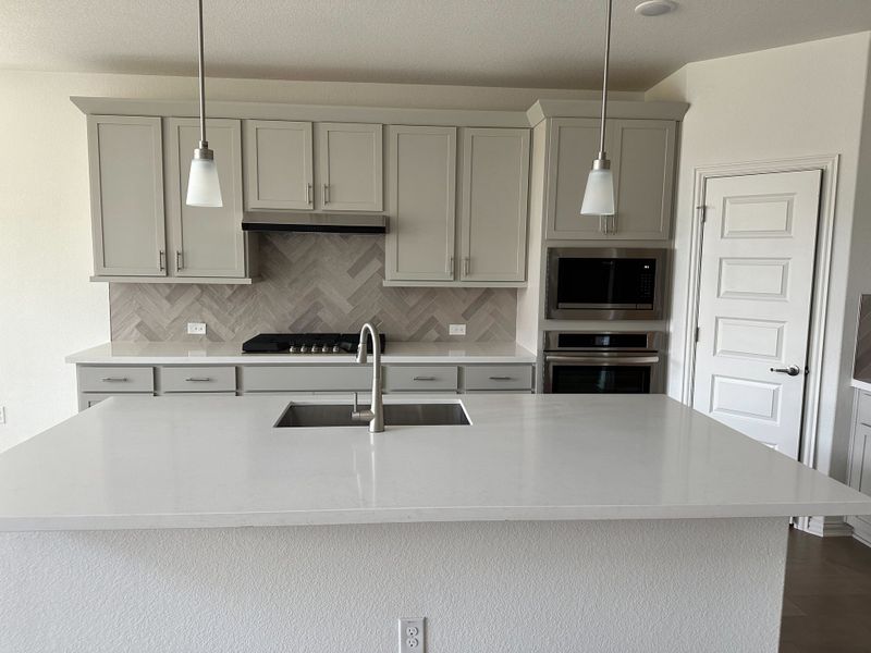 A modern kitchen featuring sleek grey cabinetry, a herringbone backsplash, and elegant pendant lighting. A modern kitchen featuring sleek grey cabinetry, a herringbone backsplash, and elegant pendant lighting.