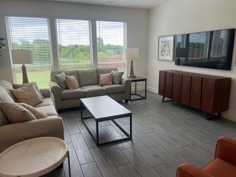 A cozy living room with large windows, sleek gray flooring, plush sofas, and a stylish wooden console with a mounted TV. A cozy living room with large windows, sleek gray flooring, plush sofas, and a stylish wooden console with a mounted TV.