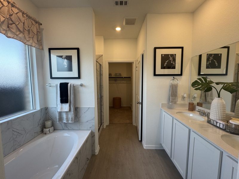 A bright bathroom featuring a marble-tiled bathtub, dual sinks, elegant decor, and a spacious feel.