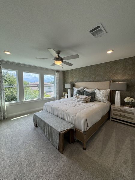 A cozy bedroom with large windows, soft carpeting, a stylish bed, and accent lighting creating a serene retreat.