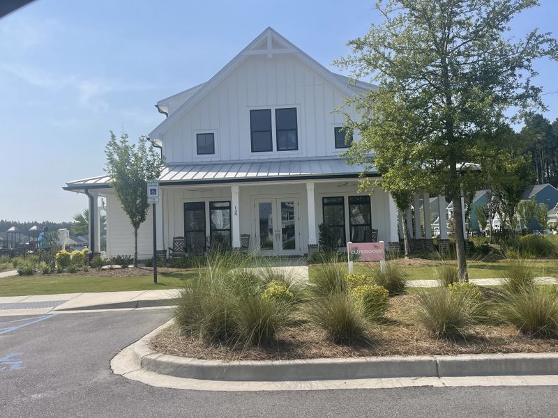 A charming white clubhouse with a welcoming porch in Homecoming by True Homes (Ravenel, SC), surrounded by manicured landscaping.
